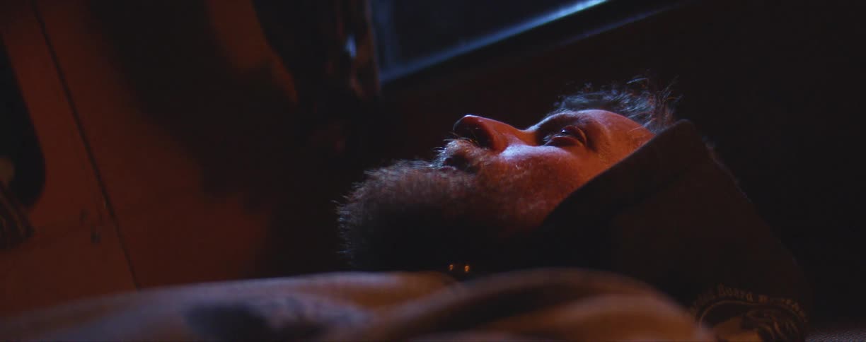 A man lying in the back of his vehicle as lights go across his face