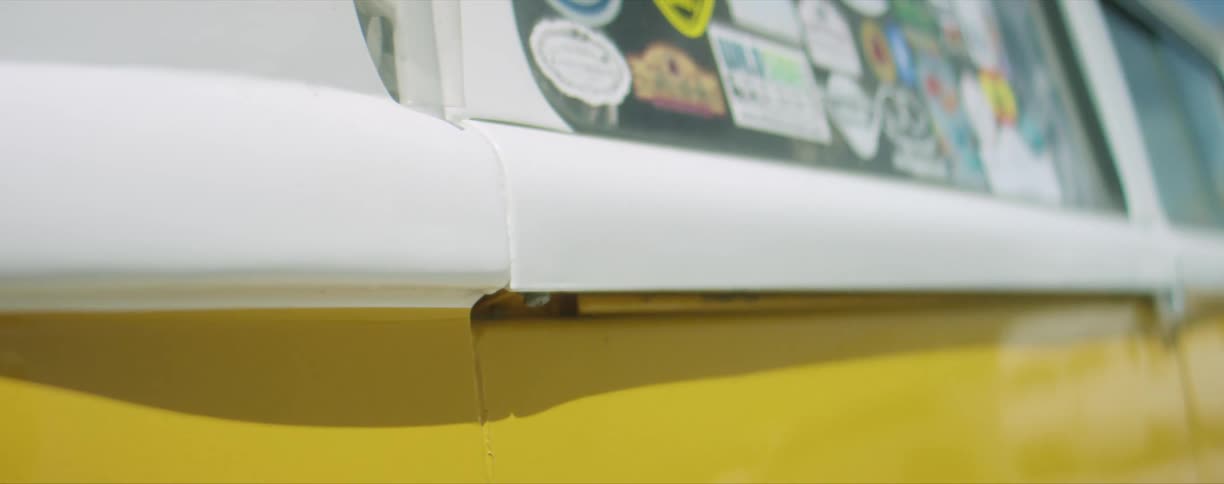 Multiple stickers on the rear window of a bright white and yellow van parked outdoors
