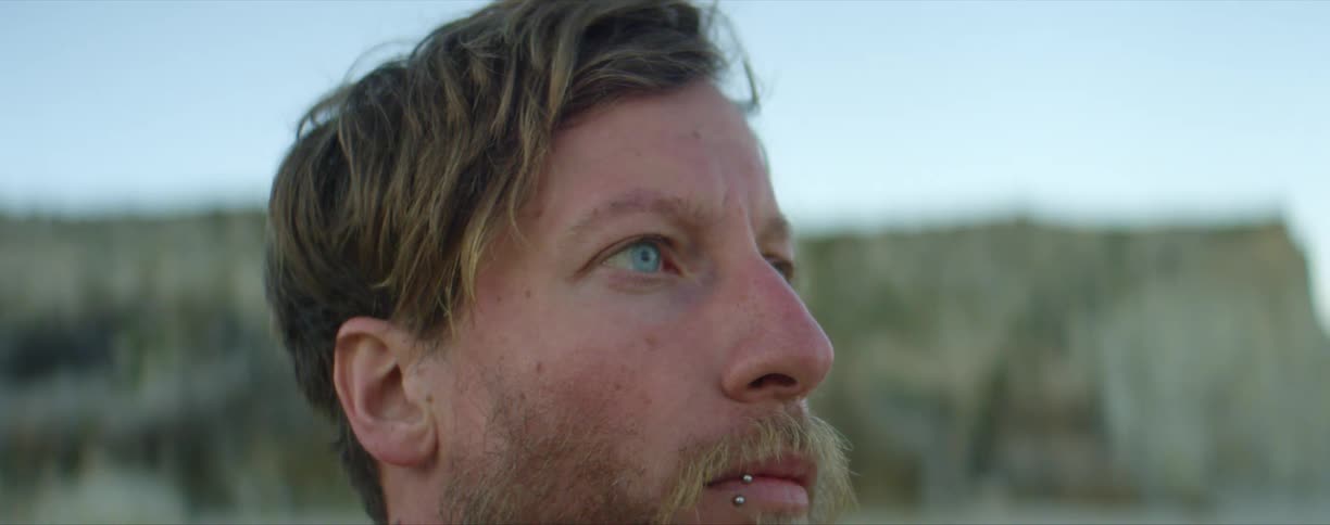 A man with blue eyes and a lip piercing outside
