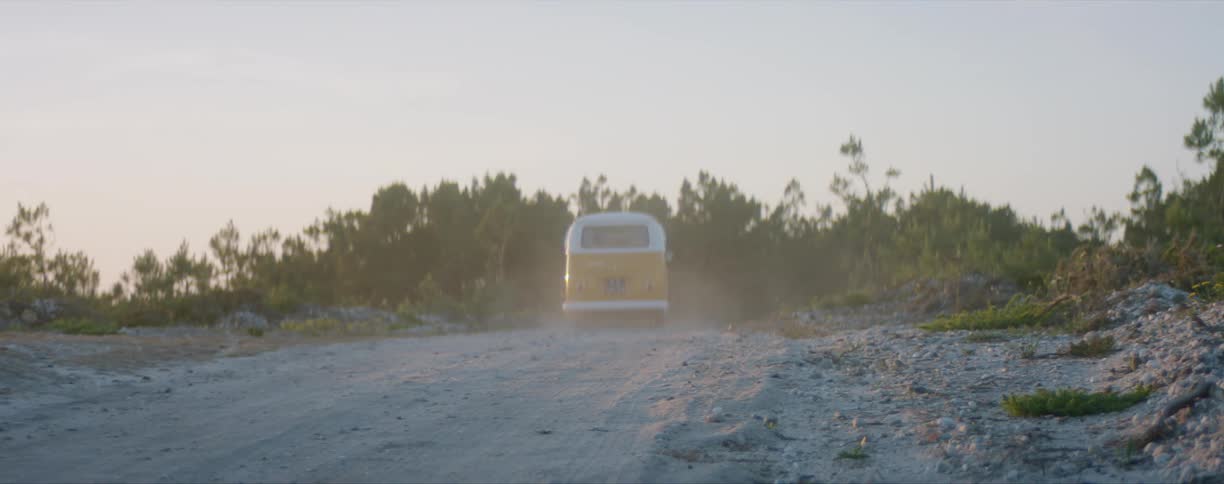 Bright white and yellow van driving on a dirt road on a the way to the beach at sunset