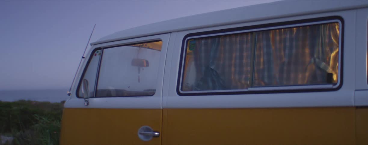 Lights inside a parked bright yellow van near the ocean at evening
