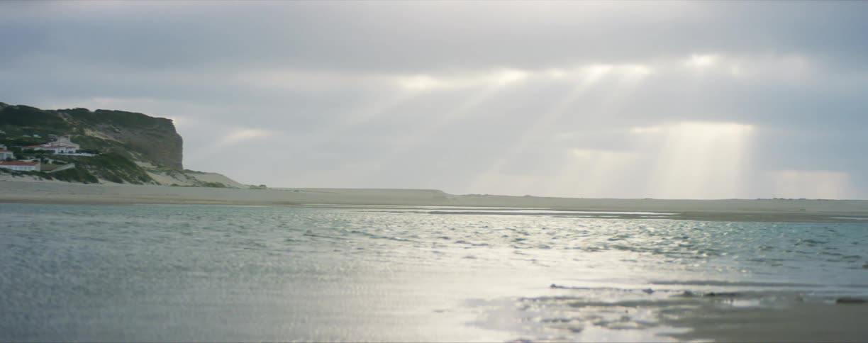 Coastline as waves roll in on a cloudy day with sun rays shining through