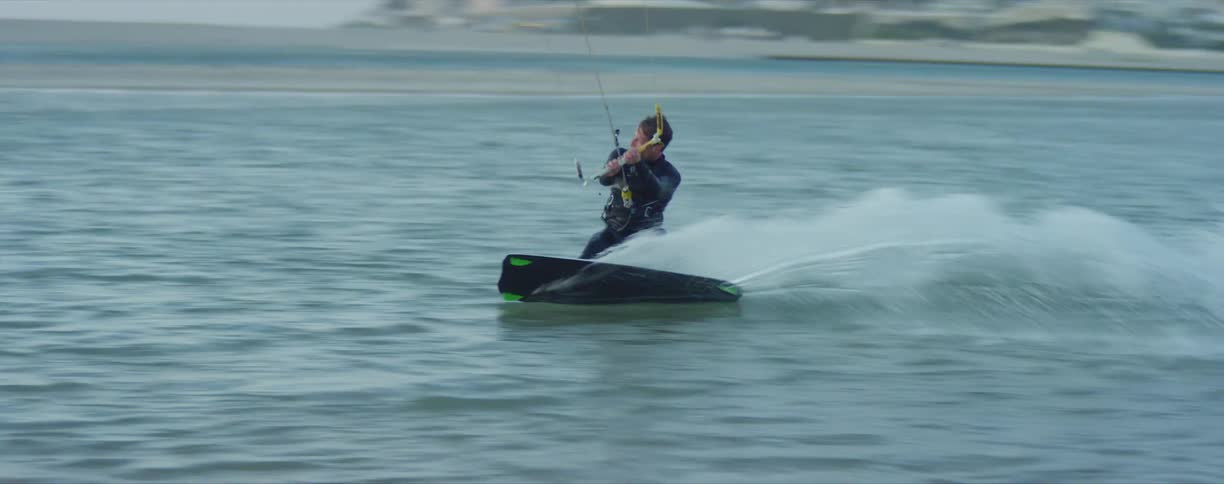 Man riding a board while kite surfing near the coast at sunset