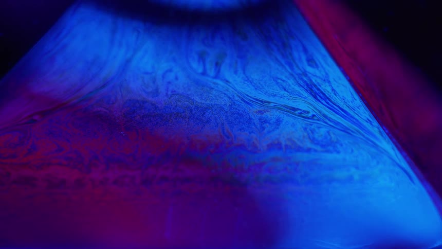 Flowing fluorescent liquid twirling in abstract shapes in a dark room under ultra violet light