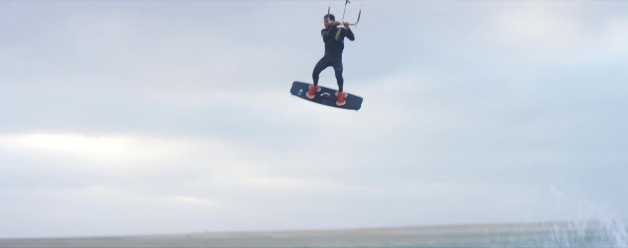 A man on a board sailing in the ocean is lifted up in to the air