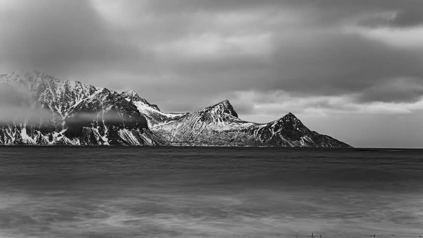 Timelapse of clouds passing over the snow covered peaks of a mountain range in the coast