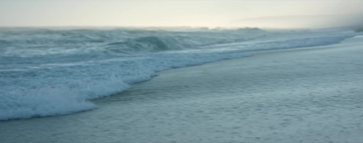A beach with waves and sand with the sky and clouds in the background