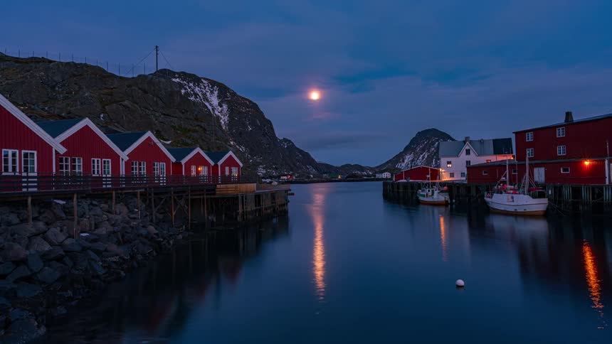 Time lapse of the moon rising over the mountains near the waterfront town