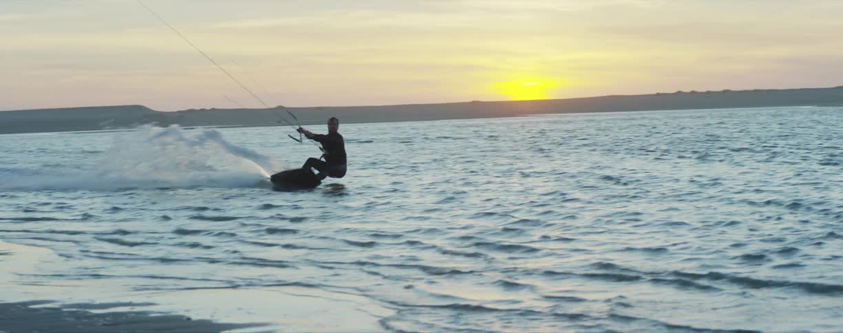 A man kite surfing on water near a coast with the sky and clouds in the background