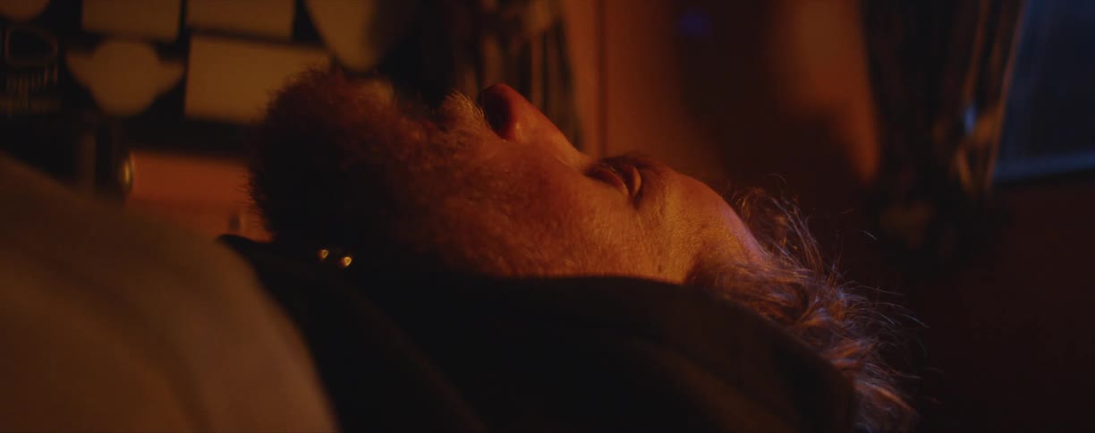 Close up of a bearded mans face laying in the floor of a dimly lit room
