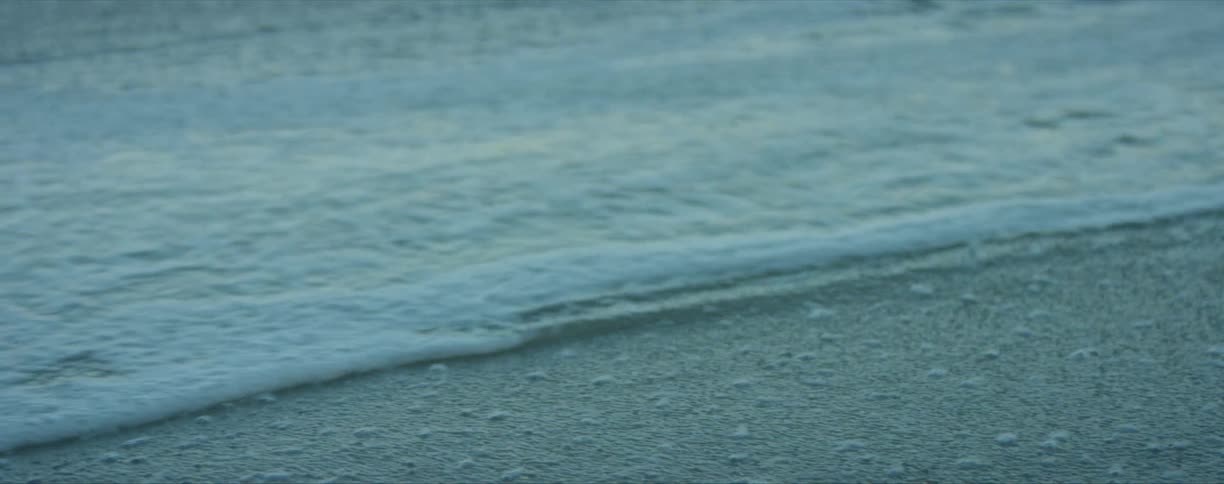 A gentle ocean wave washes into a sandy beach during the day