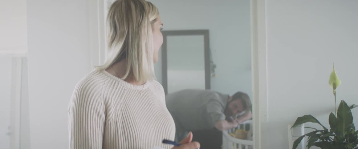 A woman turns to talk to a man who is leaning over a crib in the next room