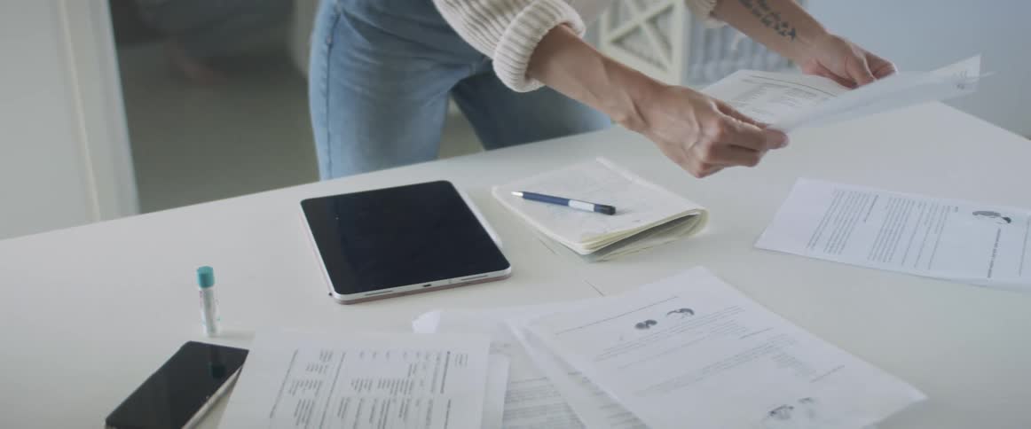 A woman stands by a table with papers a pen and a tablet