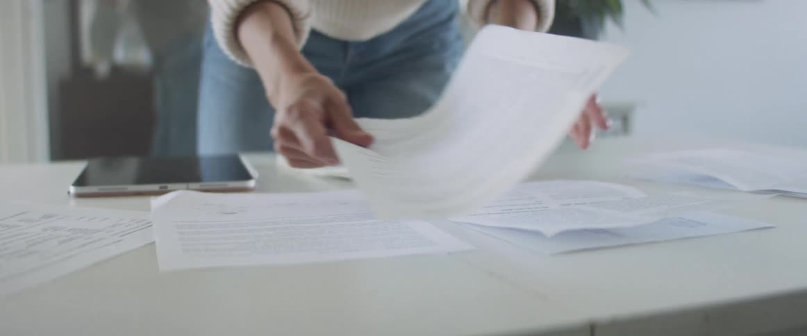 Woman with jeans and a white knit sweater sorts papers into groups on a table