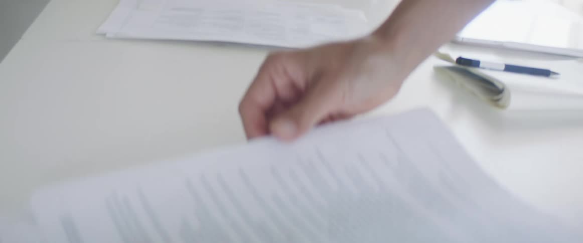 A woman looks at paperwork on a table and writes in a notebook