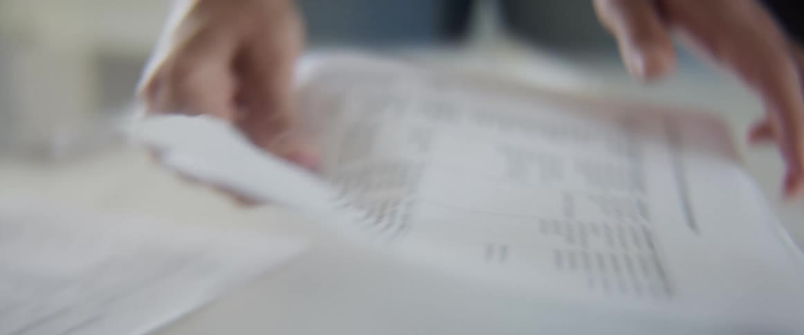 A person searches through stacks of papers on a desk in the daytime