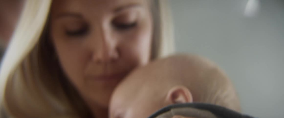 A woman cuddles her son and then another person puts a soother in his mouth