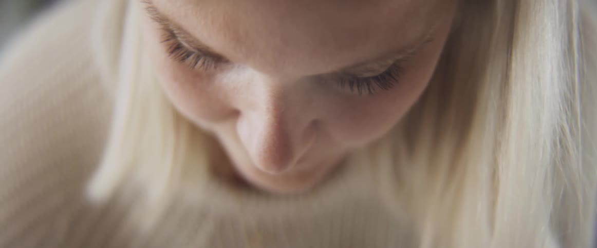 Blonde woman with a white knit sweater looks down
