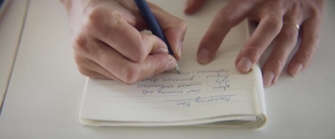 A person sits at a table and writes in a notebook about a management plan