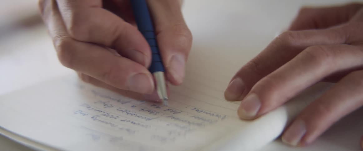A person hand writing on a notebook using a blue ink pen