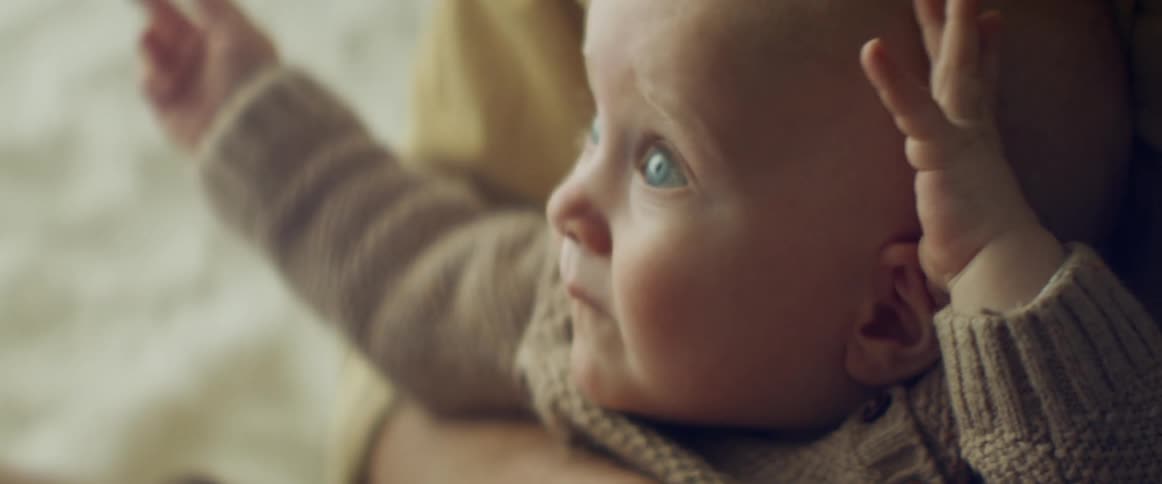 A baby sitting and waving arms with another person
