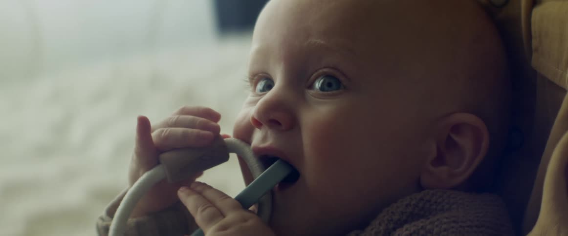 A cute little teething baby gnaws on a plastic toy as its being held
