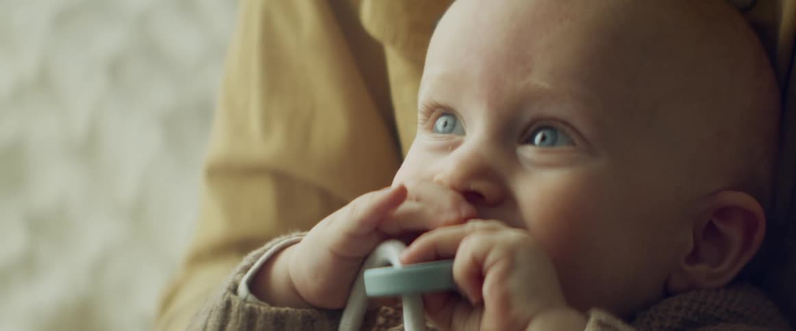 A baby bites a teething ring while being held by their father outdoors