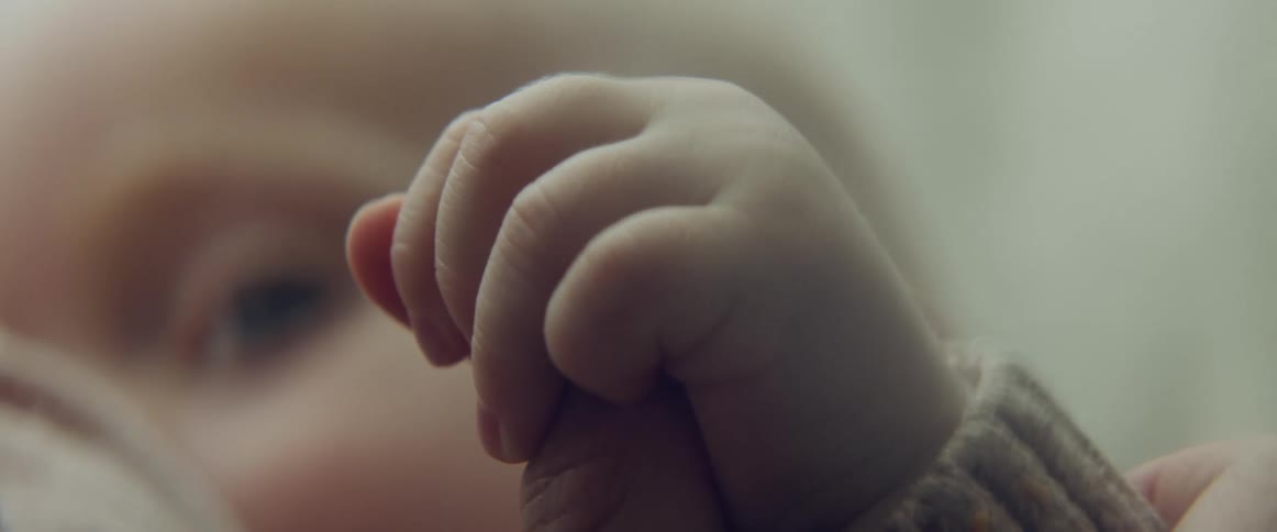 Baby holds mothers finger with a full hand while breastfeeding