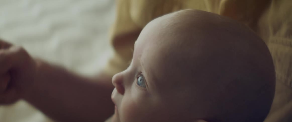 A baby boy sitting on his moms knee looks up at her