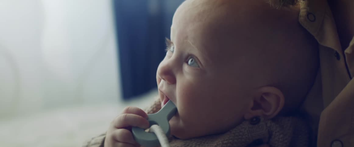 A baby sitting on the lap of a woman with a toy in his mouth