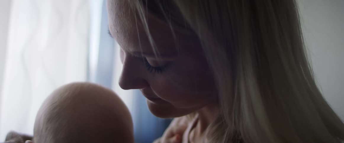 A woman holding her baby leans forward and kisses his head
