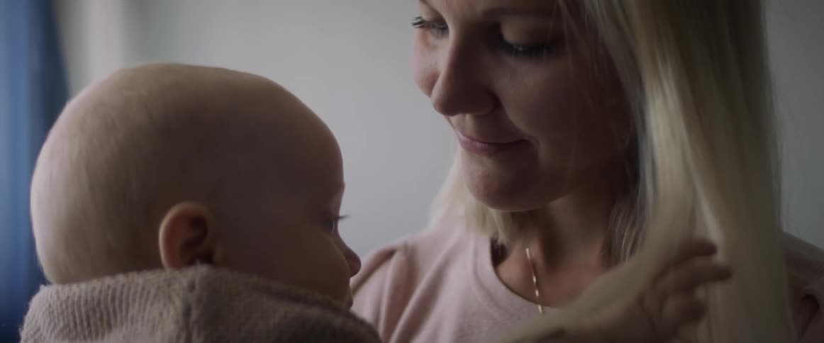 Baby plays with the necklace of her mother in a room at home