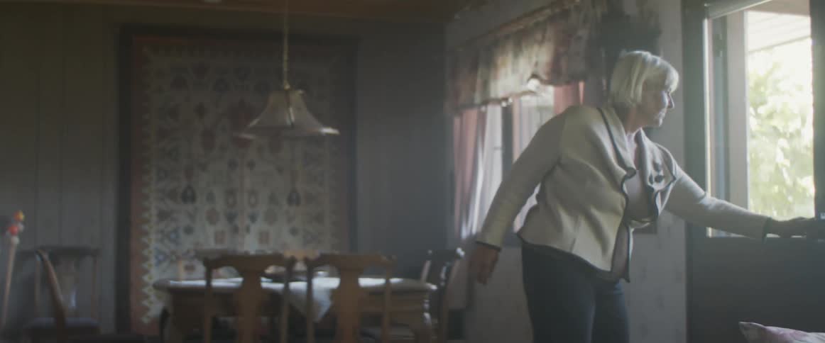 A woman sitting on a couch standing up opening the door and greeting a man a woman and a baby