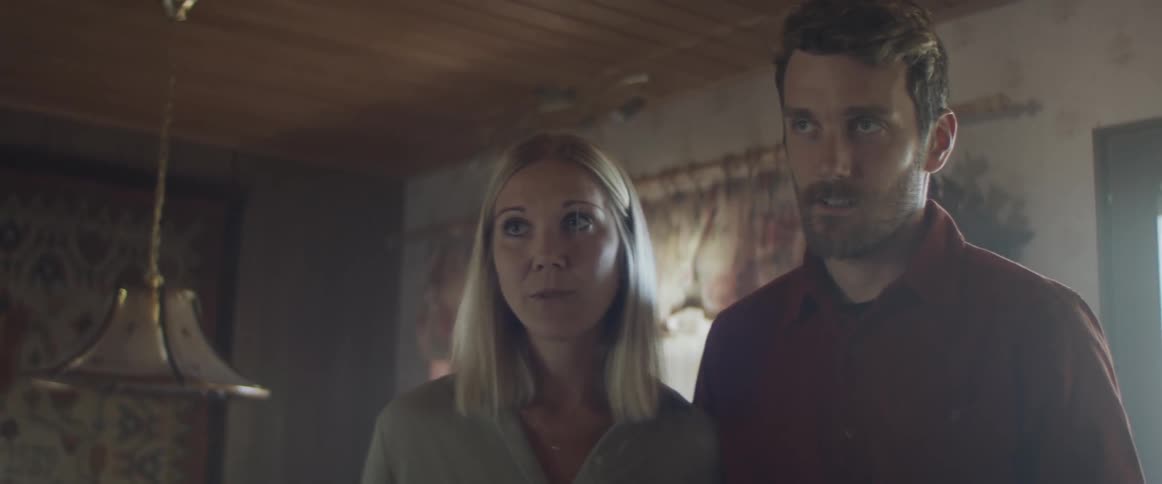A man and woman stand together in the living room of a house walking talking to an older woman standing across from them