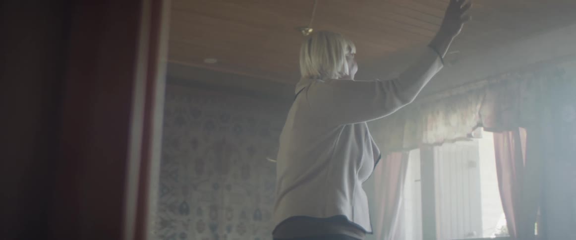 Senior woman smiles and waves from the living room of her home
