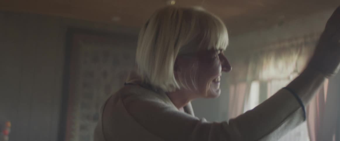 Senior woman walks into the living room and waves smiling at someone outside the house