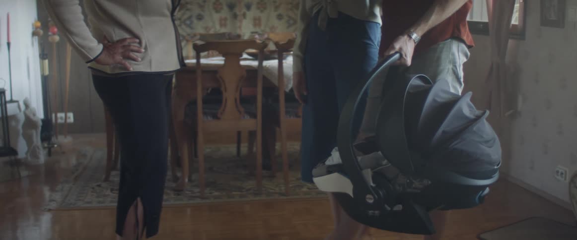 A man and woman stand in front of another woman holding an infant carrier in a home