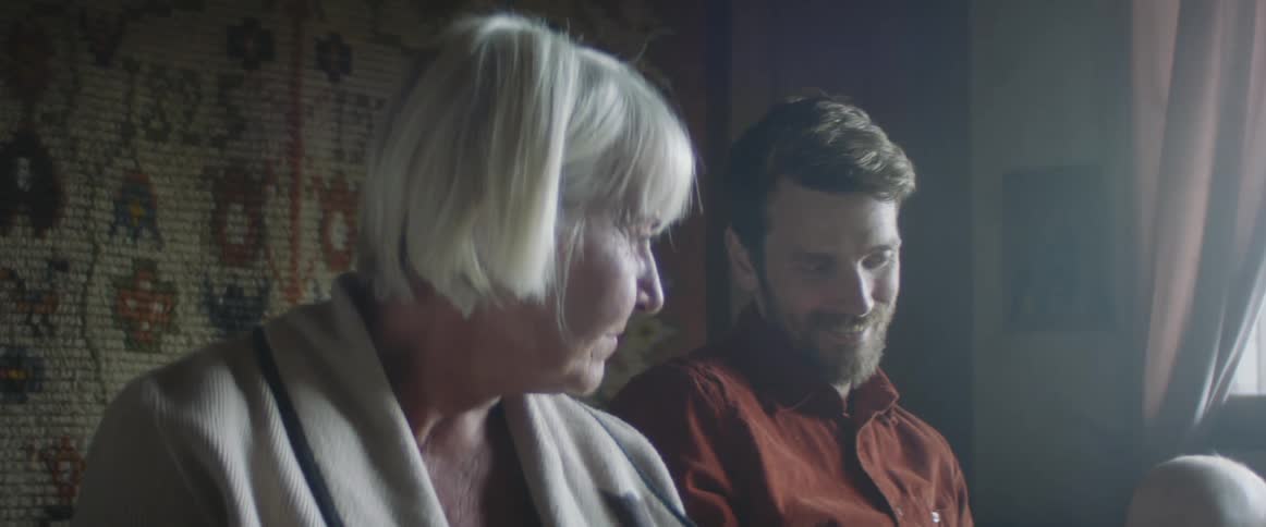 An elderly woman sits next to her son and grandson and they talk and laugh