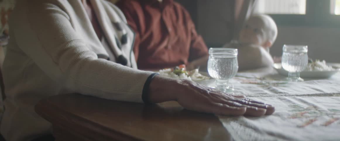 A man holding a baby sits at a table next to an elderly woman and another woman reaches her hand across and puts her hand on the elderly womans hand