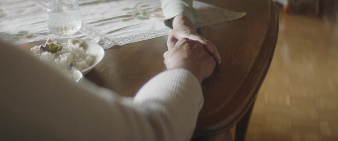 One person reaches across a dining table to gently grip the hand of the person sitting on the other side