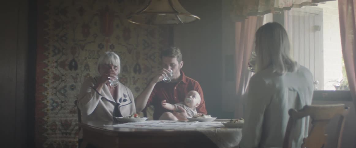 Three adults clink their drinking glasses together before drinking as they sit around a dining table with a baby during the day