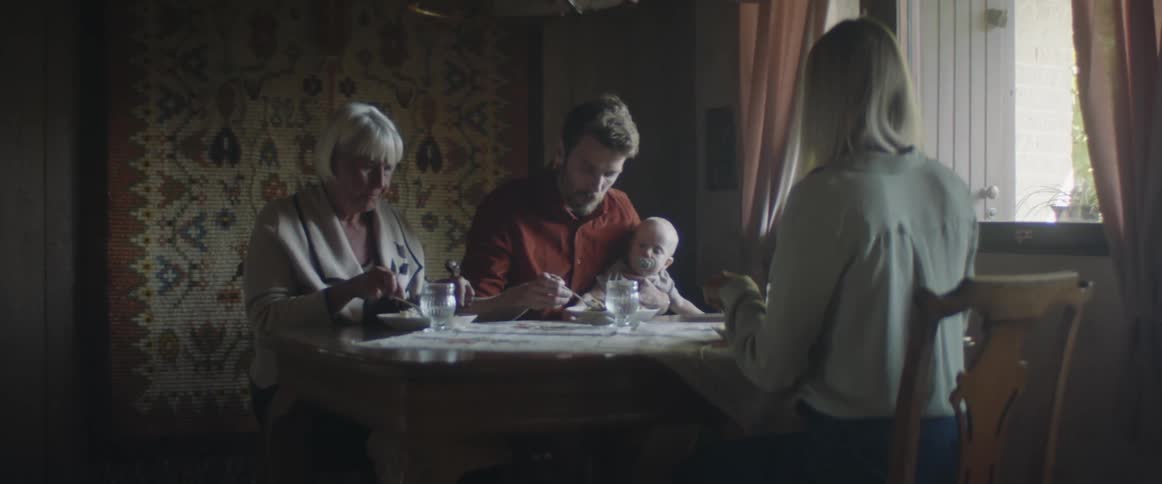 A couple sit at a dinner table with an infant and an older woman