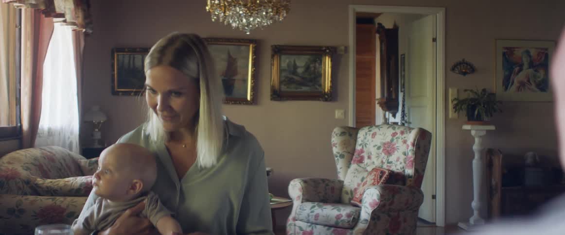 A woman holds a baby in her lap as she sits at a dining table across from an older woman