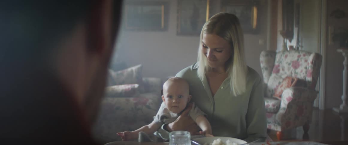 A woman sits at the table with her son on her lap as his dad shakes a toy at him from across the table