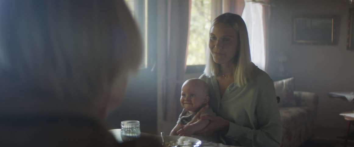 A woman sits holding a baby taking to another person in a home