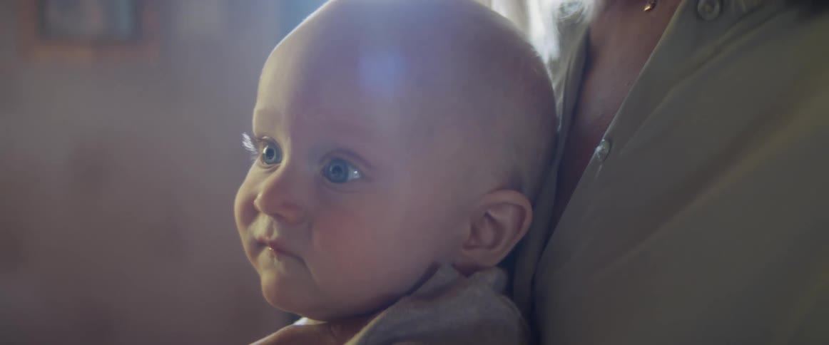 Blonde mother with a shirt holds her baby son on her chest