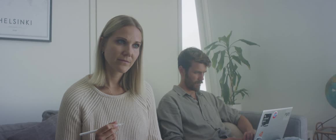 Woman sitting in the couch at home with her couple while thinking and working on a tablet