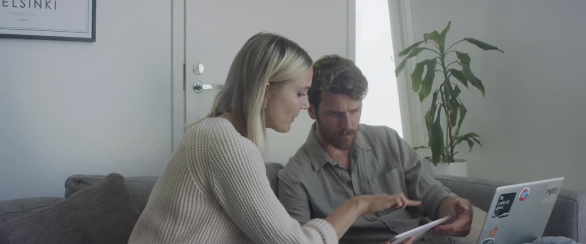 A man and a woman sitting on a couch while looking at a tablet