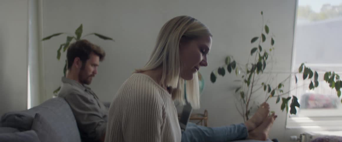 A caucasian male and female sitting on a couch relaxing and the female is texting