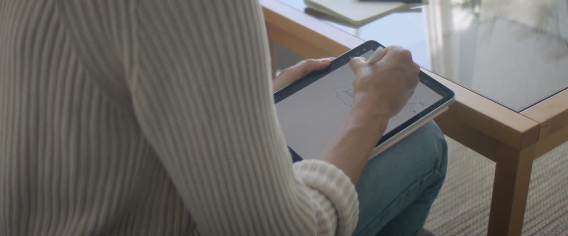 Woman with a white knit sweater and jeans sitting on a couch uses a tablet in the living room